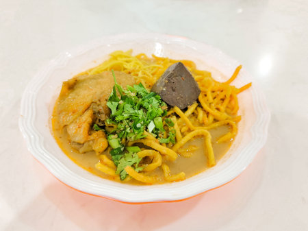 Northern Thai style curry noodles soup with chicken in a white bowl on table. Khao Soi Recipe.の写真素材