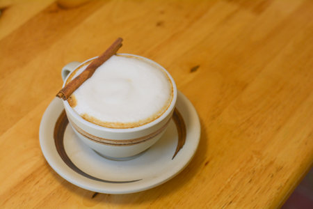 Hot cappuccino in a white cup with cinnamon bark on a wooden table.の写真素材