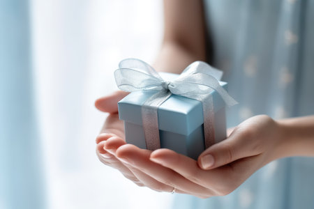 Witness the embodiment of love and thoughtfulness in this close-up image, as a female hand presents a beautifully adorned blue gift box, a heartfelt gestureの素材