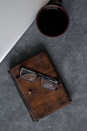 Brown leather notebook, pen, laptop and glasses on gray background.の写真素材