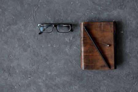 Brown craft leather notebook, pen and glasses on gray background.