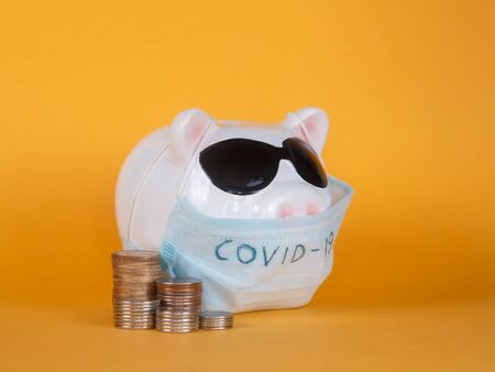 Covid-19 financial crisis. Coronavirus crisis, white piggy bank with face mask stuffed with coin on...