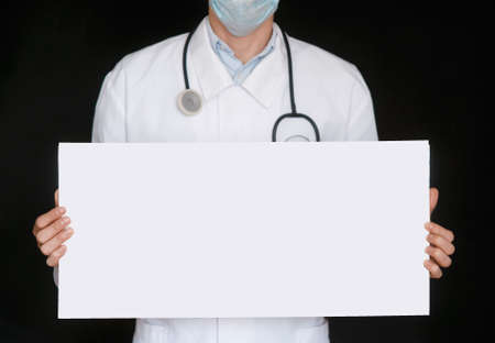 A man in a black t-shirt and medical gloves holds a white sheet of paper. Mockup. Coronavirus. Quarantine . Epidemic. Copy space. Warning. Doctor's hand in blue glove holding sheets of paper.の写真素材