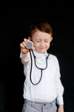 Smiling little boy in medical uniform playing with stethoscope Black backgroundの写真素材