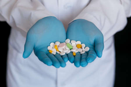 Many small white pills in the hands of a doctor wearing medical blue disposable gloves. Hands take one pills.の写真素材