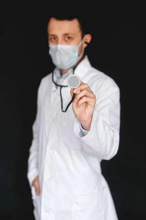 Male Doctor on a black background with a stethoscope in his hands close-up.の写真素材