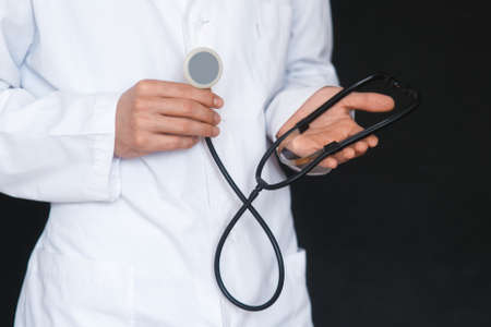 Male Doctor on a black background with a stethoscope in his hands close-up.の写真素材