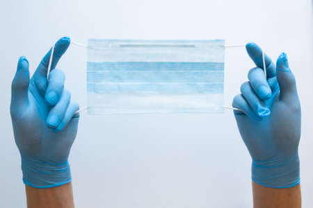 First person view of a woman holding face mask over white table background. Protective raspiratory mask for spreading virus. Close up, copy space, top view, flat lay.の写真素材