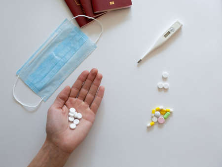 In the hands of the doctor is an electronic thermometer for measuring temperature, a protective mask from coronavirus and tablets, medications on a blue background .COVID-2019の写真素材