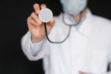 Male Doctor on a black background with a stethoscope in his hands close-up.の写真素材