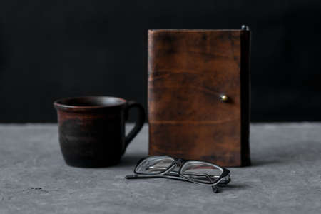 Brown leather notebook and glasses on wooden table. Businessman workspace with cup of black coffee. Business planning and work day organization. Coffee break at workplace in office.の写真素材