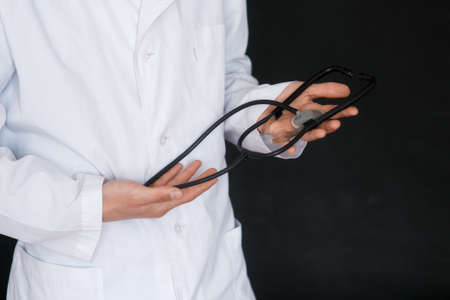 Male Doctor on a black background with a stethoscope in his hands close-up.の写真素材