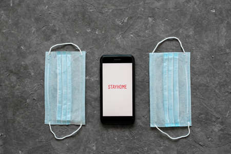 The concept of staying at home is the epidemic of the coronavirus covid-19. Antiseptic face mask and phone on a white background. View from above copy space.のeditorial素材