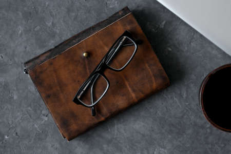 Brown leather notebook, pen, laptop and glasses on gray background.の写真素材
