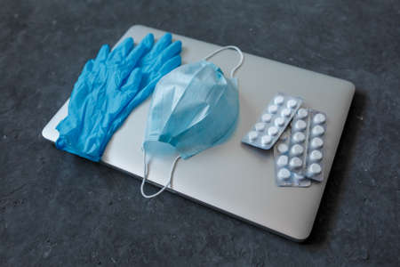 Robot at home during coronavirus epidemic. laptop with protection against covid-19 close-up mask for face medical gloves and tablets on a gray background .の写真素材