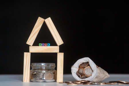 Glass bank with many world coins, house word or label on money jar and wooden home geometric blocks...