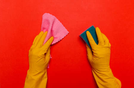 Hands in rubber yellow gloves wipe the surface with a pink rag and a purple sponge on a yellow background. place for text.の写真素材
