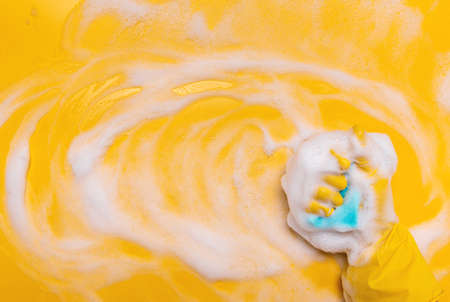 wipe the foam on a yellow background with a blue gloved sponge.の写真素材