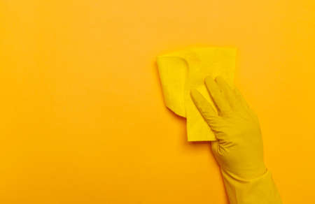 a hand in yellow gloves holds a yellow rag on a yellow background. place for text.の写真素材