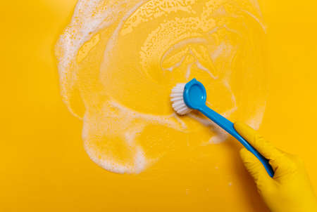 wipe the foam on a yellow background with a blue gloved brush.の写真素材