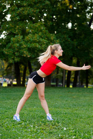 A young blonde girl is engaged in sports in the park, a woman does a warm-up in the street. Active outdoor trainingの写真素材