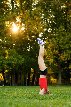 A young girl practices yoga in nature. woman performs a headstand in a park. Concept - healthy,...