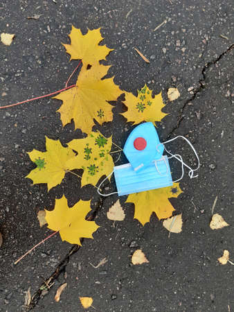 Coronavirus autumn. Yellow maple leaf, respirator and disposable medical mask on wet asphalt. Virus....