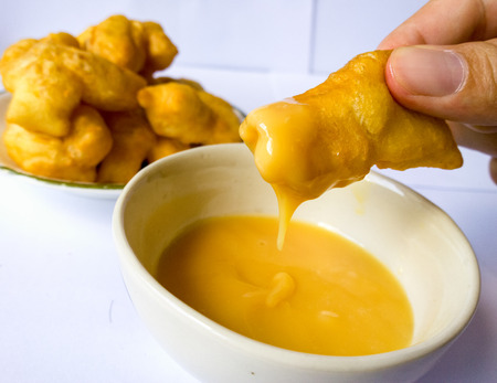 Dipping deep-fried dough stick in sweettened condensed milk sauce,close-up の写真素材
