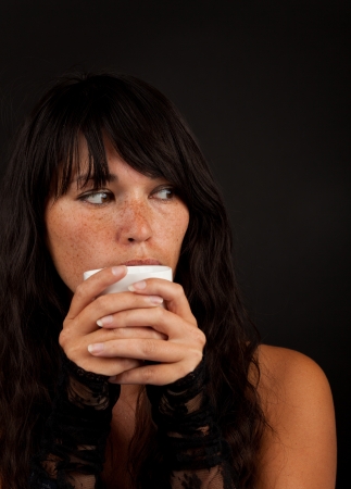 beautiful young woman holding a cup of coffee on black backgroundの写真素材