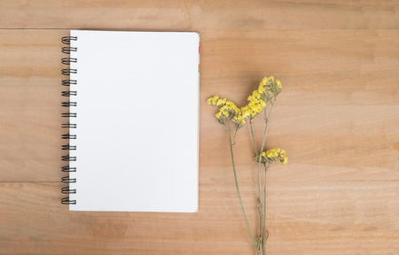 Empty no line note book and yellow flowers on offce desk wooden background. View from above with...