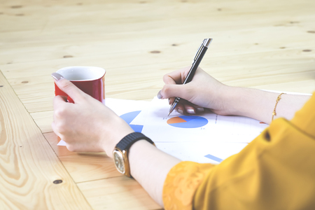 Hand of businesswoman point the goal chart and holding red cup of coffee when working.の写真素材
