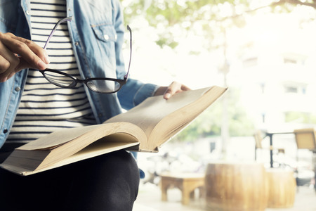 Woman use glasses to read a book in library cafe in the morningの写真素材