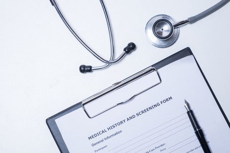 The topview of doctor desktop with stethoscope, clipboard with medical records form and penの写真素材