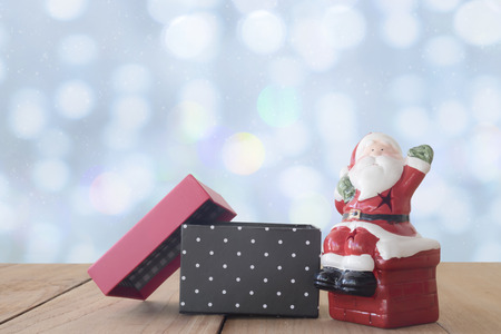 Santa Claus doll and open gift box on wood table on bokeh and snow white dropの写真素材