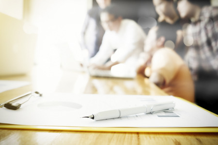 Closeup pen on business marketing report and blur of young man and woman startups business meeting...
