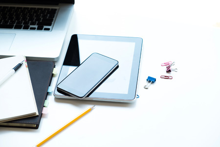 Computer, tablet , mobile phone, notebook, pen and pencil are on white office table. Technology and...