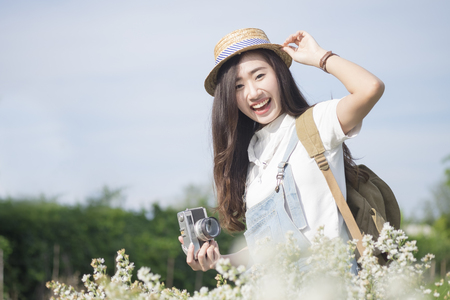 Asian hipster cute teen girl with camera in white flower garden,  vintage tone travel and relax with nature concept.の写真素材