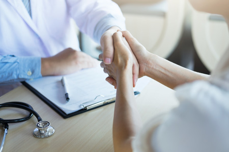 Male doctor in white coat shaking hand to female colleague. Patient filling thankful to doctor.の写真素材