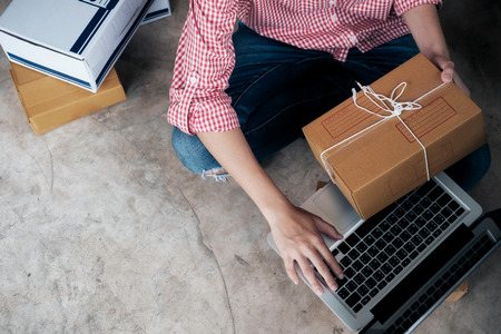 Young business start up online seller owner using computer for checking the customer orders from email or website and preparing packages for product office equipment.の写真素材