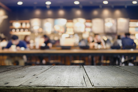 Empty wooden table for present product on coffee shop or soft drink bar blur background with bokeh image.の写真素材