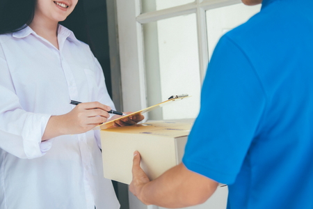 Signing to get package. Young woman receiving parcel from delivery man