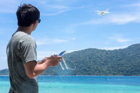 Young man navigating a flying drone with remote control. Man in seaside flying drone and taking pictures.の写真素材