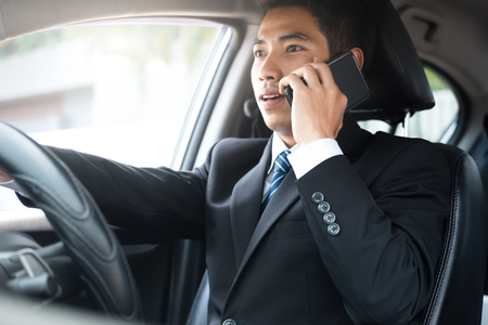 Young businessman talking on his smart phone with serious face while driving the car. Important...
