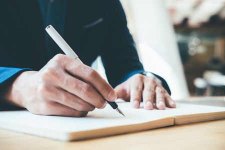Businessman writing notebook on office desk table close up. Business concept.の写真素材