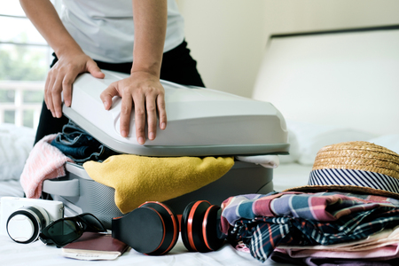 Preparation for vacation or travel. Packing his clothes and stuff into large opened suitcase that almost already full.の写真素材