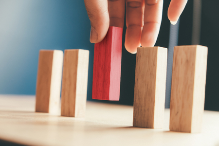 Human resource and Business concept in choose idea person from many candidate and different. Close up hand pick one of red wood block from many wood block in row.の写真素材