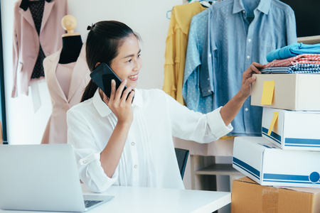 Young business start up online seller owner using computer for checking the customer orders from email or website and preparing packages for product office equipment. の写真素材