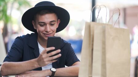 Young man with shopping bags is using a mobile phone while doing shopping.の写真素材