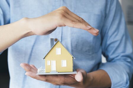 Businessman hand hold the house model saving small house. House insurance.の写真素材