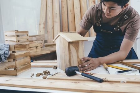 DIY woodworking and furniture making and craftsmanship and handwork concept. Carpenter working on woodworking machines in carpentry shop. Young man working as carpenter and taking wood stock.の写真素材